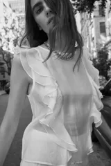 Blusa blanca semitransparente de cuello redondo y sin mangas, con volantes en los hombros y en el frente.