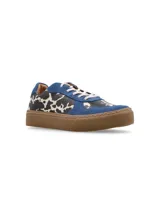 Zapatillas bajas con estampado de vaca en blanco y negro, detalles en gamuza azul y suela marrón.