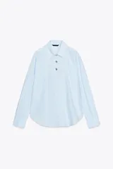 Camisa celeste a rayas verticales, de popelín, con cuello solapa, manga larga y cierre frontal con botones dorados.
