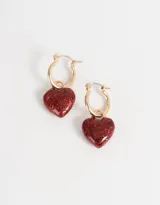 Aros tipo argolla dorados con dije de corazón cubierto de glitter rosa.