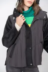 Campera negra con mangas de lana y cuerpo de nylon acolchado, con capucha y cierre frontal con botones a presión.