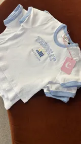 Remera crop blanca de algodón elastizada con cuello y mangas con ribete celeste. Bordado frontal con la palabra "URUGUAY" y la bandera uruguaya. Marca Coppelia.