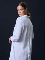 Vestido camisero blanco de algodón con cuello solapa, escote en V y mangas 3/4 regulables. Presenta bolsillos laterales verticales y abertura con botones en la espalda.