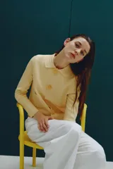 Chaqueta de punto color amarillo pálido, con cuello solapa y manga larga. Tiene bolsillos delanteros de plastrón y cierre frontal con botones con forma de flor.