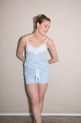 Pijama de short y musculosa color celeste con textura acanalada. La musculosa tiene escote en V con detalle de puntilla blanca y tirantes finos blancos. El short tiene elástico y lazo blanco en la cintura.