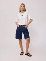 Remera gris de algodón con corte cropped y calce holgado. Tiene cuello redondo y mangas cortas con costuras reforzadas en color coral. Presenta un pequeño logo de la marca Rusty en el pecho.