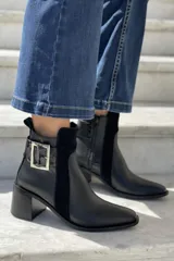 Botas cortas de gamuza color marrón topo, con punta fina, taco de madera y hebilla decorativa plateada.