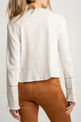Blusa blanca de algodón con escote en V, cierre con lazos, mangas largas con puños elásticos y detalles de encaje y volados.