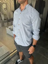 Camisa de hombre a rayas verticales celestes y blancas, con cuello mao y mangas largas. Cierre frontal con botones de madera.
