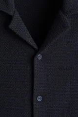 Camisa azul marino de manga corta en tejido de punto con textura. Tiene cuello resort, tapeta con botones y corte recto.