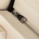 Cartera grande tipo shopper color beige, confeccionada en rafia y cuero sintético. Tiene doble asa de mano, correa bandolera regulable y cierre superior. El interior está forrado en tela de algodón y poliéster, y cuenta con un bolsillo con cierre y dos bolsillos abiertos.