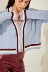 Cardigan celeste de punto trenzado, con escote en V y botones metálicos. Presenta ribetes a contraste en cuello, puños y bajo.