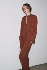 Camisa marrón de Zara Woman Collection confeccionada en hilatura con mezcla de lyocell. Tiene cuello redondo, manga larga acabada en puño, bajo asimétrico con aberturas laterales y cierre frontal con botones.