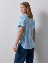 Blusa de algodón estampado a rayas verticales en tonos celeste, azul y verde. Tiene cuello a la base, escote en V con bordado y botones. Terminación de ruedo con nudo.