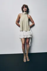 Falda pantalón negra de tiro bajo con cintura drapeada y bajo acabado en volantes superpuestos. Presenta un lazo largo y fino que cae desde el lateral.