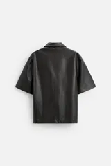 Sobrecamisa negra de manga corta confeccionada en tejido efecto piel, con cuello solapa, bolsillo frontal de parche y cierre frontal con botonadura oculta.