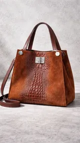 Bolso tipo tote bag de gamuza color marrón óxido, con panel central de cuero con textura de cocodrilo en tono marrón oscuro. Posee asas superiores de cuero marrón oscuro y una correa de hombro desmontable a juego. El cierre principal es metálico tipo pestillo.