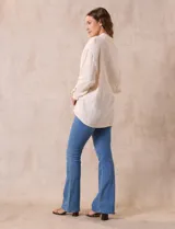 Camisa blanca de algodón con textura arrugada, cuello con solapa, abertura central con botones y bolsillo aplicado en el pecho. Mangas largas con largo regulable mediante presilla y botón.