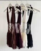 Vestido corto negro con escote halter profundo y detalle de encaje o red en el torso. La falda es corta y con textura. Se combina con botas altas negras de cuero sintético.