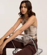 Top halter de tela satinada, color beige con efecto tie-dye/manchas en tonos marrones. Presenta detalles de encaje en el escote y el bajo. El diseño es ajustado al cuerpo.