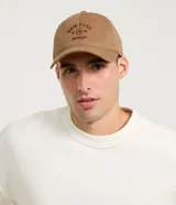 Gorra de sarga color beige con visera curva, bordado frontal con la inscripción "New York 1996 Brooklyn" en marrón. Ajuste trasero con hebilla metálica.