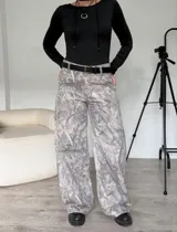 Pantalón jean gris con estampado abstracto, tiro bajo, corte wide leg y cinturón negro.