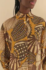 Camisa con estampado de conchas marinas en tonos mostaza y marrón, de corte holgado, mangas largas y cuello clásico.