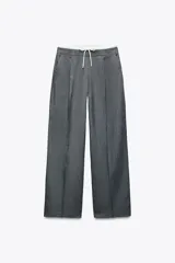 Pantalón gris de tiro alto con doble cintura elástica ajustable con cordón y tejido combinado. Pinzas frontales, bolsillos delanteros y falso bolsillo de vivo en espalda. Pernera ancha.