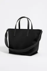 Bolso shopper mediano Bimba y Lola color negro, con doble asa de mano y correa bandolera ajustable y extraíble. Presenta un parche rectangular con el logo de la marca en la parte frontal.
