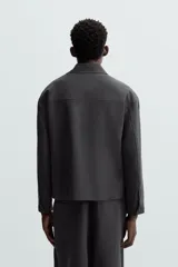 Sobrecamisa negra de corte amplio, con cuello solapa, manga larga con puños abotonados, bolsillos de parche en el pecho, bolsillos laterales y cierre frontal con botones.