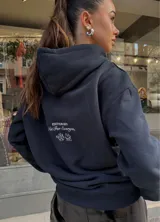Hoodie negro de corte holgado con capucha y cordón ajustable. Estampado frontal con la leyenda "BE TRENDY EST. 2022" en color rosa.