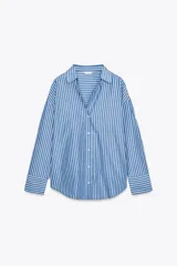 Camisa celeste con rayas verticales blancas, de corte holgado, cuello solapa, escote pico y mangas largas con puños abotonados.