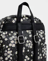 Mochila negra con estampado de margaritas blancas, confeccionada en cuero sintético. Cuenta con correas regulables, manija superior, acceso con cierre, bolsillo frontal con cierre y tag de cuerina. Incluye un pouch extraíble.