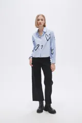 Camisa celeste a rayas verticales blancas, con cuello clásico, cierre frontal con botones y estampado de corazones negros.