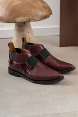 Bota corta color borgoña con textura de reptil, puntera fina, elástico negro en el empeine y talón descubierto.