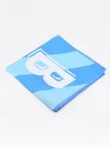 Toalla de playa de microfibra celeste con diseño de bloques de color y una letra B blanca en el centro.