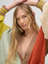 Cardigan largo color crema con detalles en color camel en el borde de los bolsillos, en el borde de los botones y en los puños. Tiene cuello en V y cierre con botones.