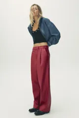 Pantalón de cuero sintético color bordó, de tiro medio, corte recto y cintura cruzada con trabillas. Cuenta con bolsillos laterales, pinzas delanteras y cierre frontal con cremallera, botón y gancho metálico.