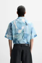 Camisa verde agua con estampado abstracto, corte relaxed fit, cuello solapa, manga corta y cierre frontal con botones.