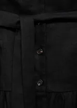 Vestido midi negro sin mangas, confeccionado en lino. Presenta escote en V, cierre frontal con botones y cinturón de lazo. La falda es acampanada con un volante en el ruedo.
