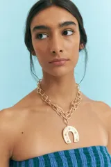 Collar dorado de doble cadena con eslabones grandes y dije de herradura con incrustaciones.