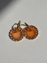 Aros colgantes con argolla dorada de acero quirúrgico y dije circular de resina color naranja con borde de strass.