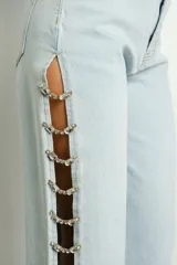 Pantalón de jean celeste con lavado claro, tiro alto, corte recto y apliques de gemas en aberturas laterales.