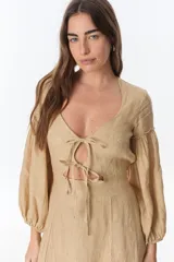 Vestido color beige de lino, con escote en V, mangas largas abullonadas y lazos frontales. Tiene corte a la cintura y falda larga con tajo frontal.