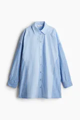Camisa oversized de algodón a rayas verticales celestes y blancas. Presenta cuello clásico, cierre frontal con botones, mangas largas con puños abotonados y hombros caídos.
