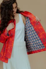 Campera tipo parka reversible con estampado de flores rojas y naranjas sobre fondo rojo, cuello marrón y bolsillos frontales.