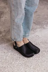 Zuecos negros de cuero con textura de pelo, diseño cerrado con hebilla lateral y tira ajustable en el talón.