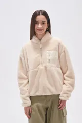 Buzo de polar tipo sherpa en color crudo, con cuello alto y cierre frontal parcial. Presenta un bolsillo de parche con cierre en el pecho y mangas largas de calce holgado.