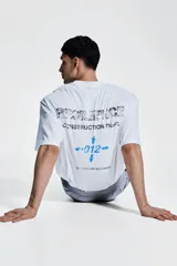 Remera deportiva blanca de corte boxy, confeccionada en tejido funcional DryMove™ que ayuda a absorber el sudor. Tiene cuello redondo ribeteado y hombros levemente caídos. Estampado en el frente con flechas y el número 012 en color celeste.