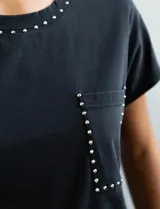 Remera gris de algodón con cuello redondo, mangas cortas y bolsillo en el pecho. Apliques de tachas plateadas en cuello, hombros y bolsillo.